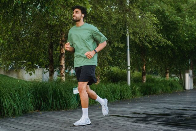 Ceas inteligent și telefon cu o aplicație de fitness deschisă, așezate pe o masă lângă o pereche de căști