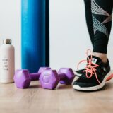 Pantofi sport, o sticlă de apă și un prosop pe podeaua unei săli de fitness, pregătite pentru primul antrenament