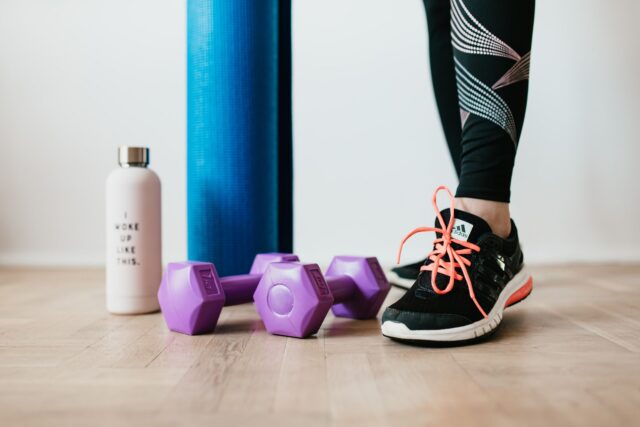 Pantofi sport, o sticlă de apă și un prosop pe podeaua unei săli de fitness, pregătite pentru primul antrenament